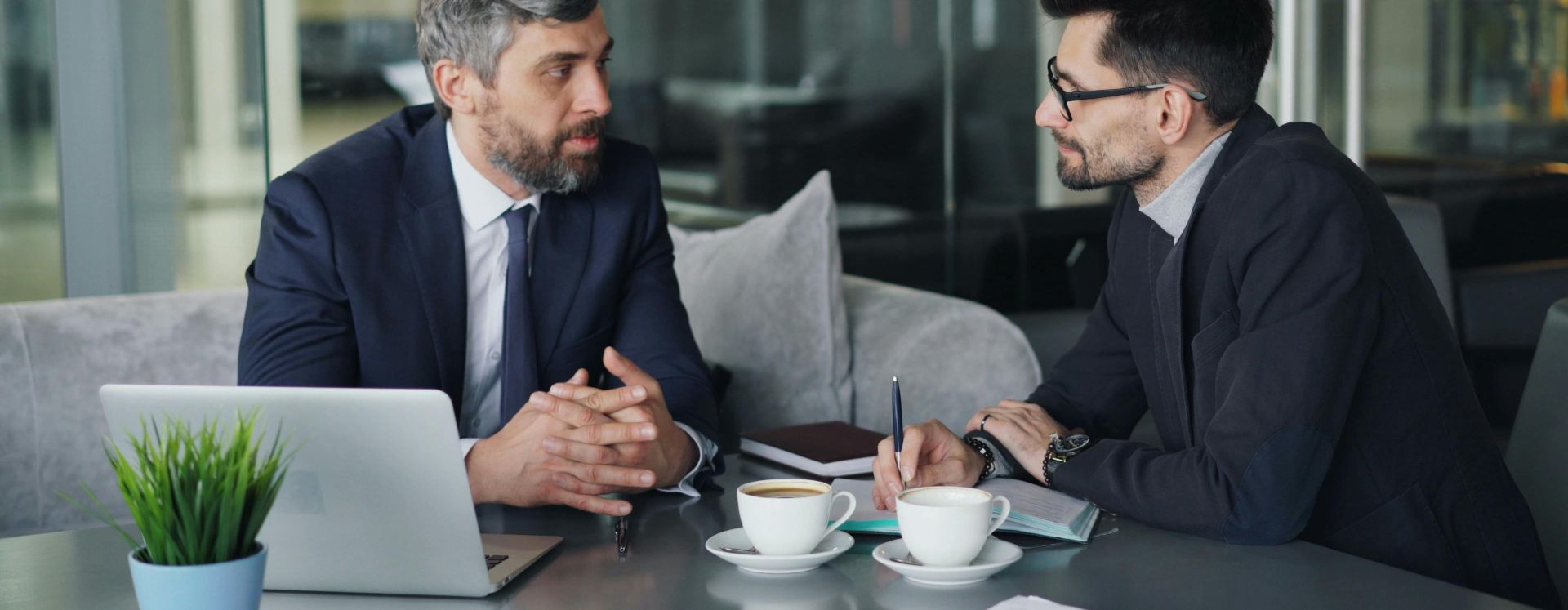 Two businessmen having a meeting with laptops, papers, and coffee at a modern office.