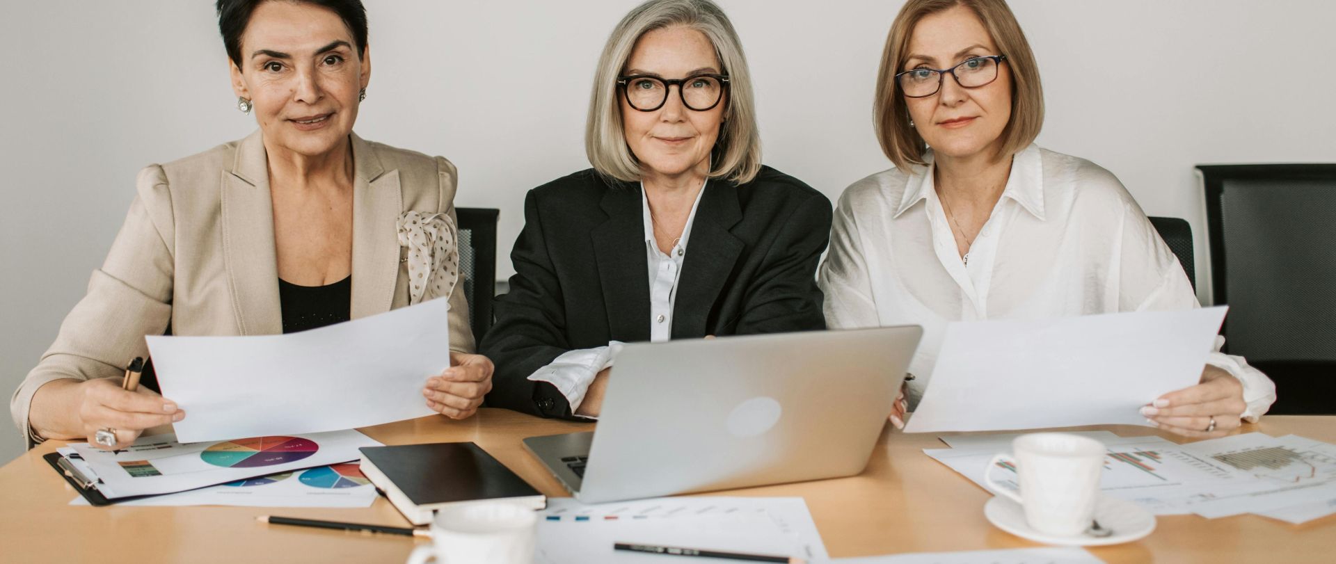 Three senior women discussing business strategies at a modern office table.