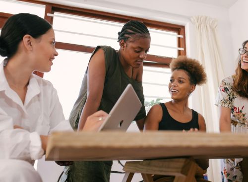 Four women in an office setting engaged in a lively creative discussion.