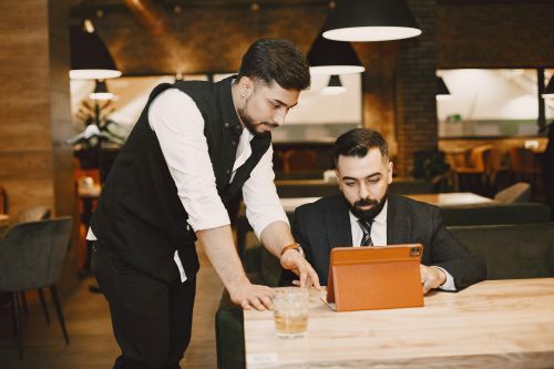 Two businessmen collaborating in a modern restaurant, discussing work on a digital tablet.