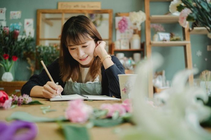 Florist in a cozy shop writing notes, surrounded by floral decor and arrangements.